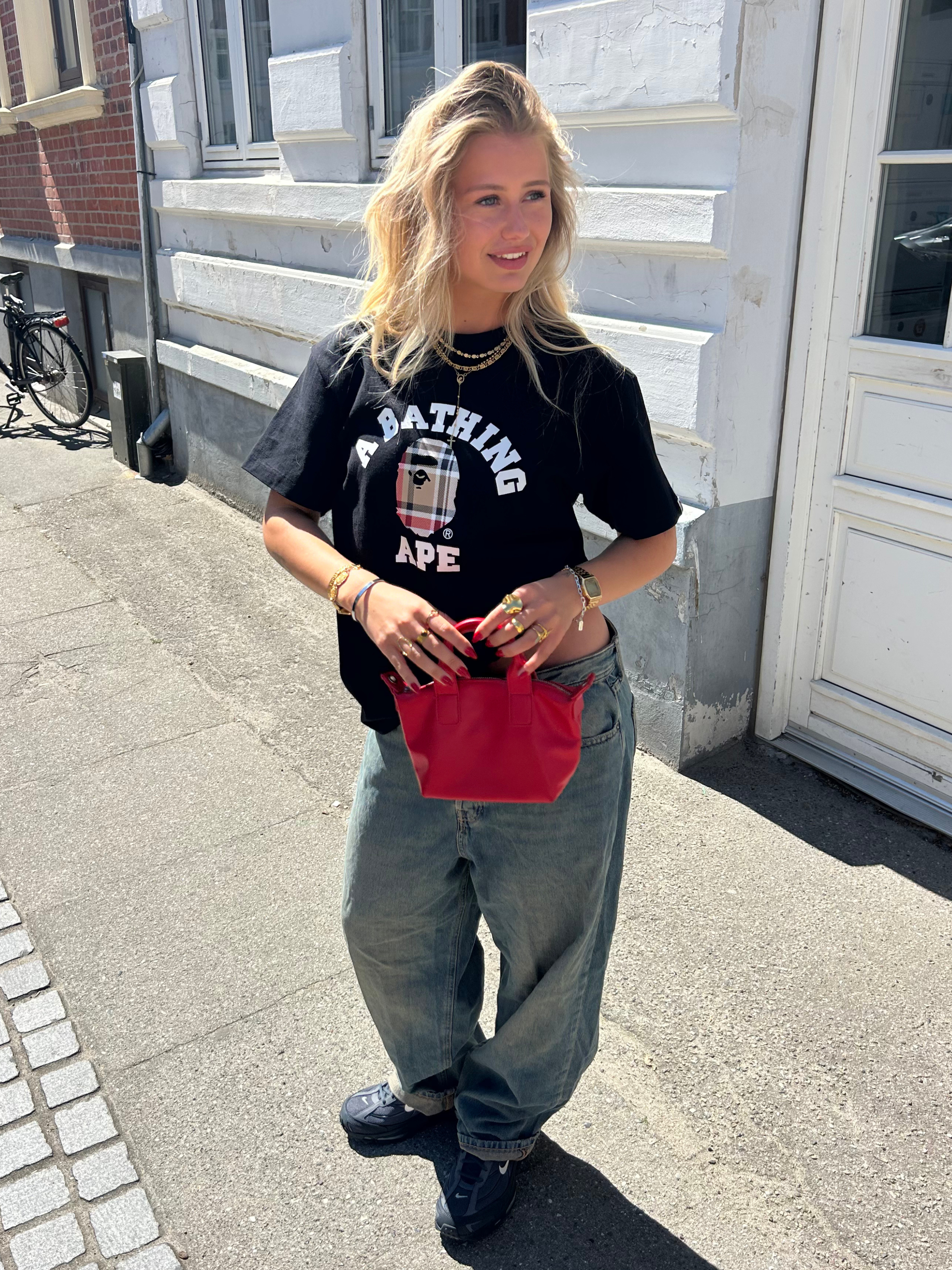 Ung kvinna i BAPE-t-shirt, vida jeans och röd väska, streetwear-mode.