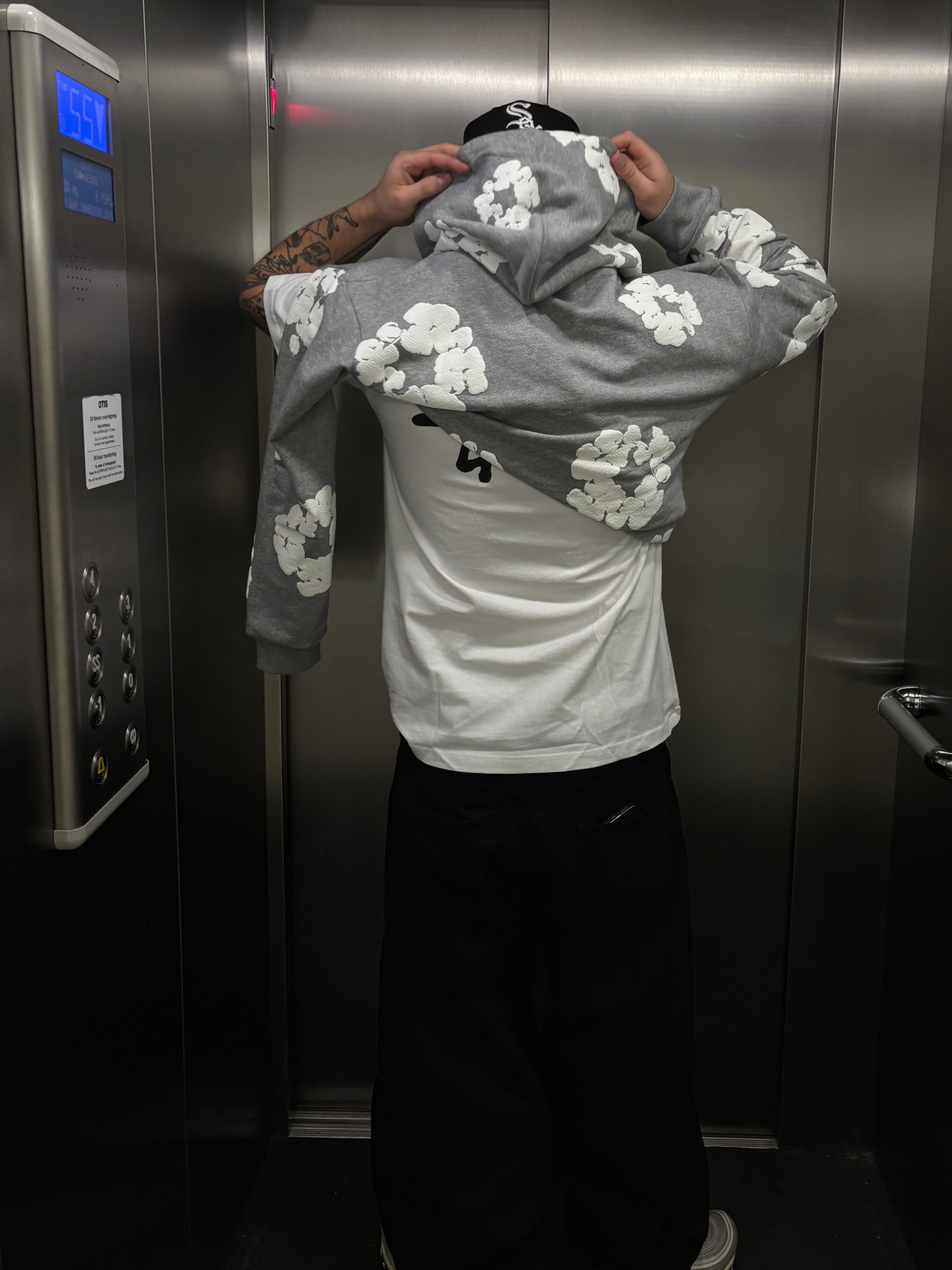 En person i hiss med grå hoodie, vit t-shirt och svarta byxor.